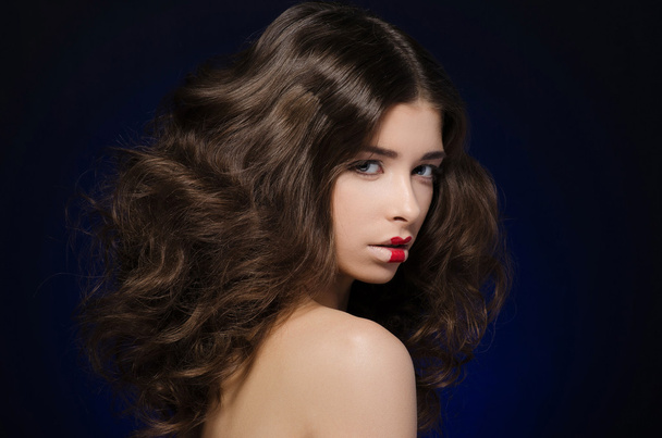 Cabello y maquillaje tema: un modelo de chica muy hermosa con pelo exuberante y maquillaje creativo sobre fondo azul
 - Foto, Imagen