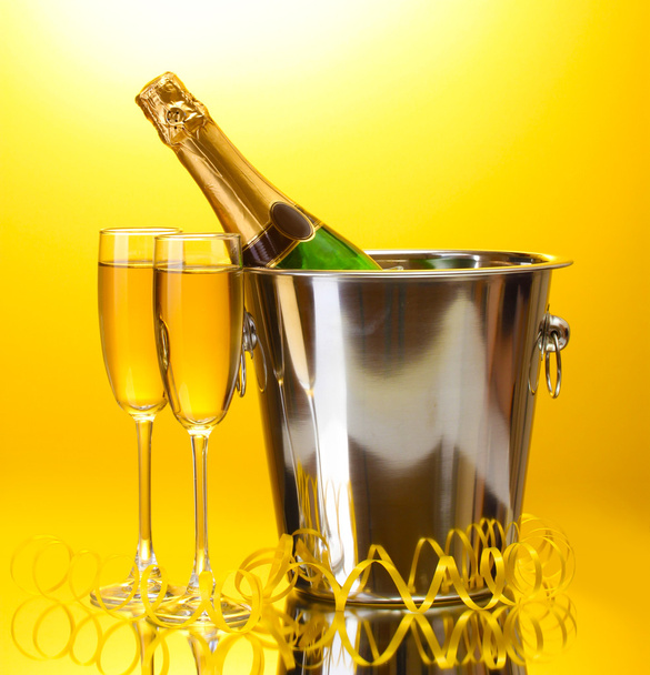 Champagne bottle in bucket with ice and glasses of champagne, on yellow background - 写真・画像