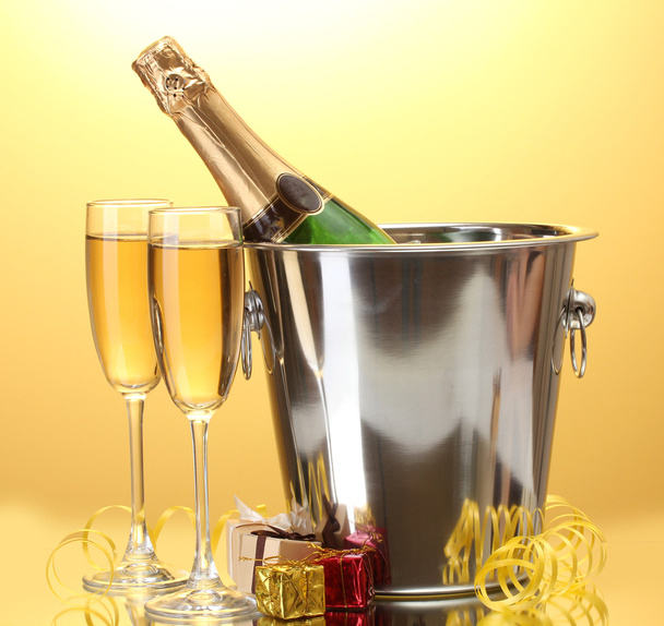 Champagne bottle in bucket with ice and glasses of champagne, on yellow background - Zdjęcie, obraz