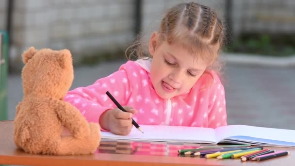 Beş yaşındaki bir kızın coşku ile onu ve onun dilini dışarı gönüllü bir sopa önünde oturan bir oyuncak ayı çizer - Video, Çekim
