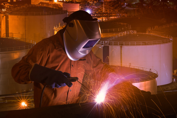 Průmyslové dělníky s bezpečnostní vybavení a ochranná maska svařování ocelových konstrukcí s zásobníky na přírodní ropy a zemního plynu a petrochemického průmyslový závod, v pozadí - Fotografie, Obrázek