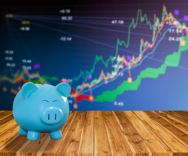 голубой копилка на деревянном фоне с размытым фондовым рынком backgrou
 - Фото, изображение