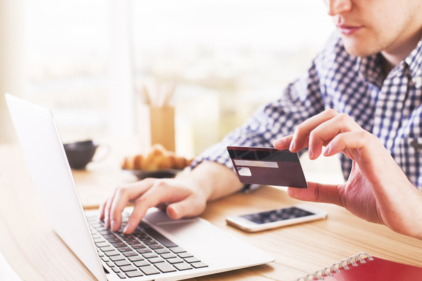 Online shopping and payment concept with male at desk typing on computer keyboard and holding a credit card - Foto, Imagen