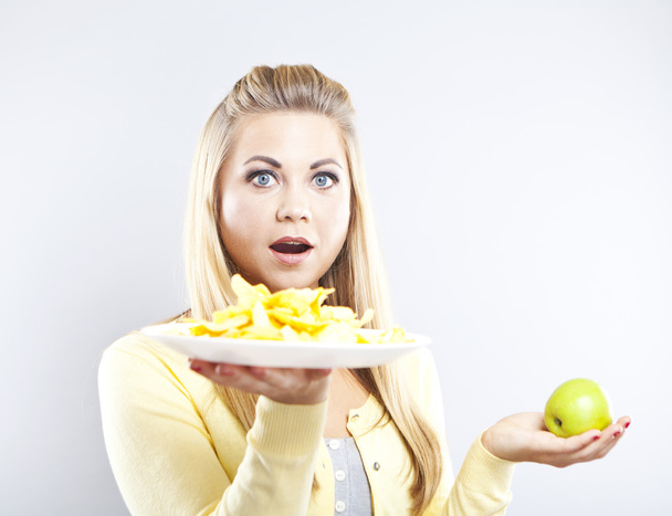 Chica rubia elige entre una manzana y patatas fritas. Comida sana y dañina. La comida deliciosa no es saludable.
 - Foto, imagen
