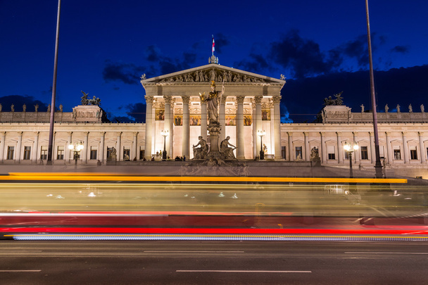 Do lado de fora do edifício do Parlamento Austríaco em Viennat à noite. O borrão de um bonde pode ser visto passando em primeiro plano. - Foto, Imagem