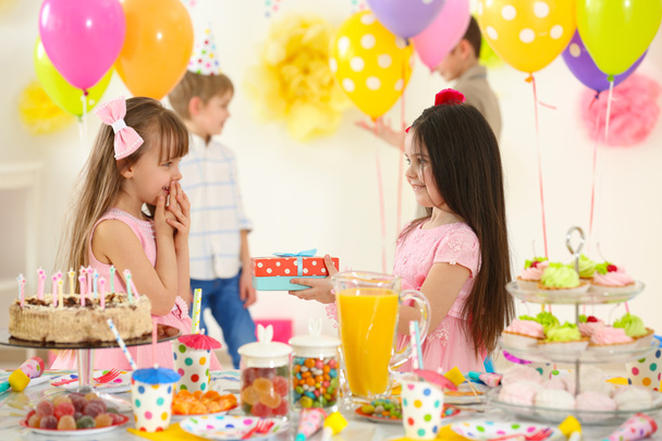Onnellinen pieni tyttö esittelee lahjan ystävälleen syntymäpäiväjuhlissa
 - Valokuva, kuva
