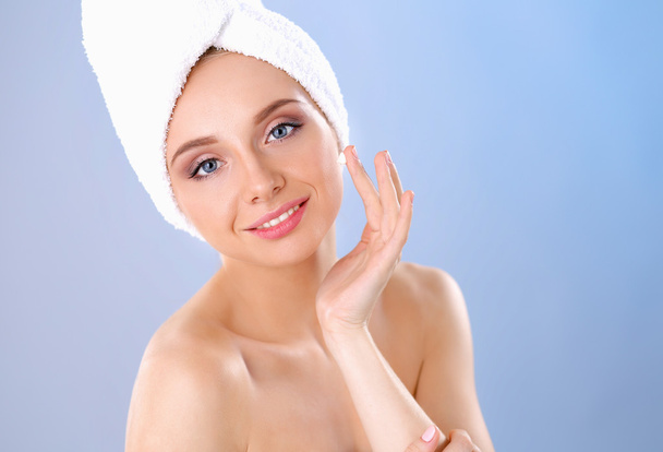 Beautiful young woman applying a creme on her face isolated on gray background - Photo, Image