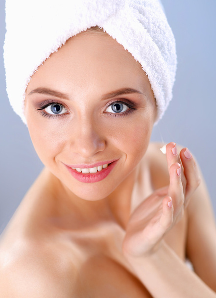 Mooie jonge vrouw, een crème op haar gezicht geïsoleerd op grijze achtergrond toe te passen - Foto, afbeelding