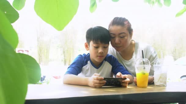 Mutter und Sohn spielen mit dem Smartphone im Garten. 4k - Filmmaterial, Video