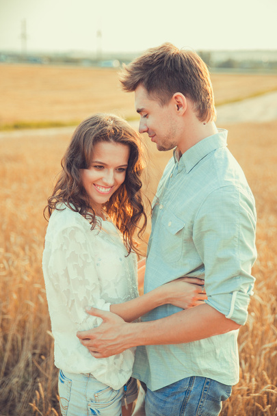 Young couple in love outdoor.Stunning sensual outdoor portrait of young stylish fashion couple posing in summer in field.Happy Smiling Couple in love.They are smiling and looking at each other - Photo, Image