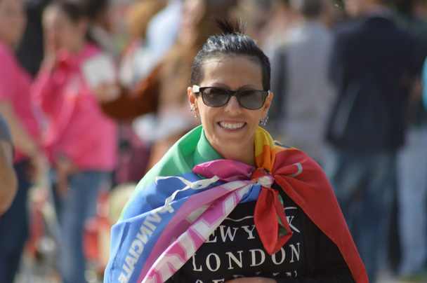улыбающаяся девушка с радужным флагом на размытом фоне и люди
  - Фото, изображение