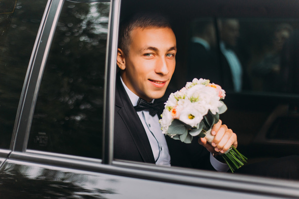 Handsome stylish groom with bouquet in the wedding car - Foto, Bild