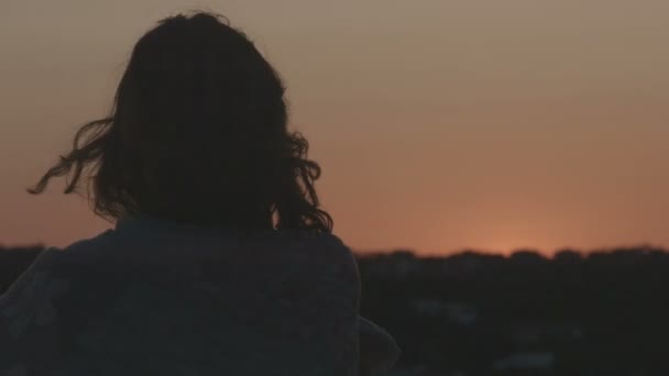 Yksinäinen nainen katselee palavaa taivasta auringonnousun aikaan. Hiukset puhaltavat tuulessa
 - Materiaali, video