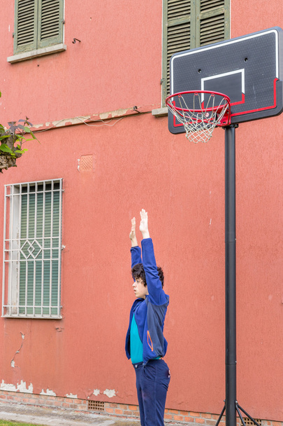 αγόρι εκπαίδευση άμυνα θέσεις σε ένα μπάσκετ γκραντζ παιδική χαρά κοντά στο ξεφλούδισμα τοίχο ενός παλιού σπιτιού - Φωτογραφία, εικόνα