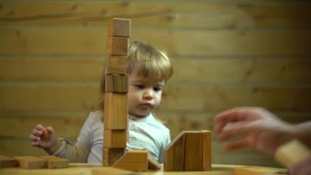 cute baby boy watches how his father constructing a toy house - Materiał filmowy, wideo