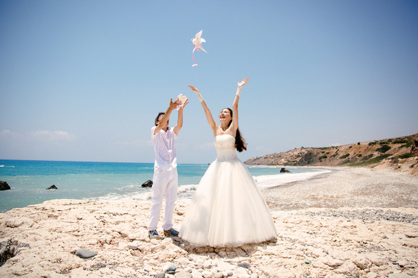 Joyeux souriant mariée et marié mains libérant colombes blanches par une journée ensoleillée. Mer Méditerranée. Chypre
 - Photo, image