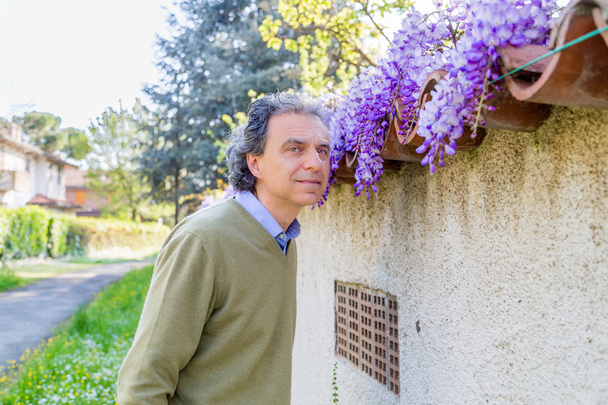 middle-aged man in light blue shirt and green sweater near wisteria plant in the countryside of Emilia Romagna - Photo, Image
