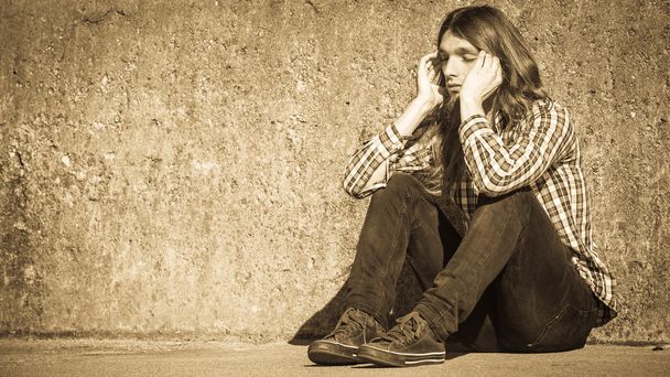 Man long haired sitting alone sad on grunge wall - Фото, изображение