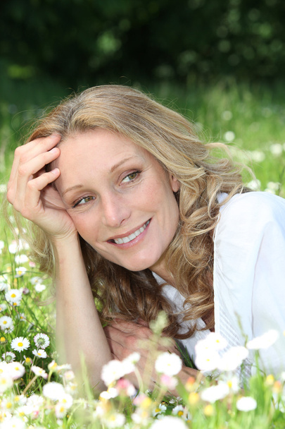 Blond woman laying in a field of daisies - Foto, afbeelding