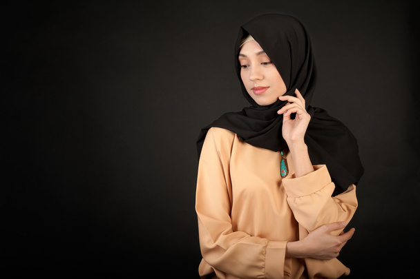photo of a young oriental woman in modern clothes with a Muslim in a scarf on a dark background - Foto, Imagen