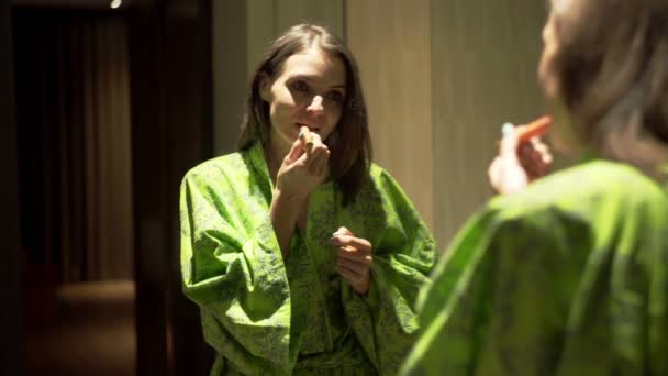 woman in bathrobe applying lipstick in bathroom - Filmati, video