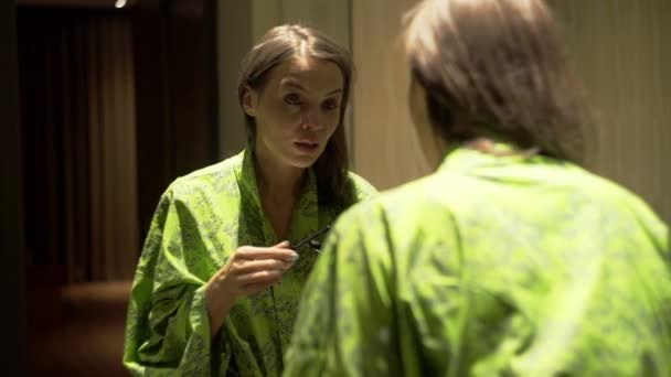 woman in bathrobe applying mascara in bathroom - Filmati, video