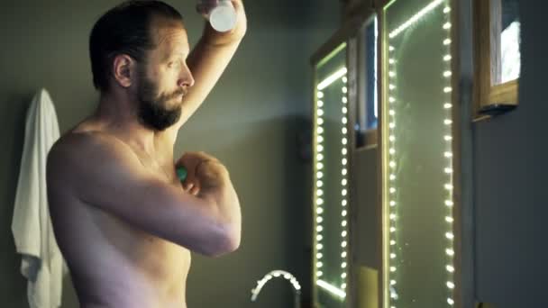 man applying antiperspirant on his armpit in bathroom - Imágenes, Vídeo