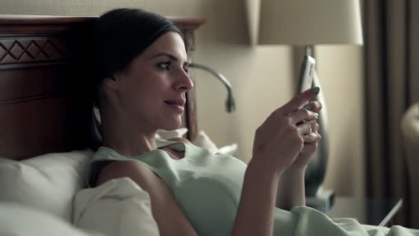 businesswoman using smartphone lying on bed  - Filmati, video