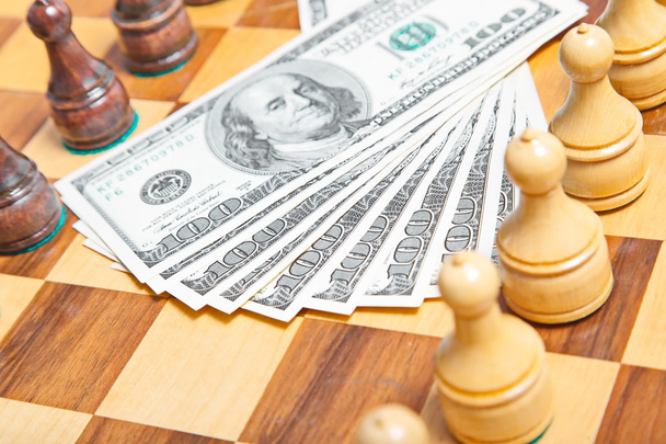 US dollars and chess figures on an old wooden chessboard - 写真・画像