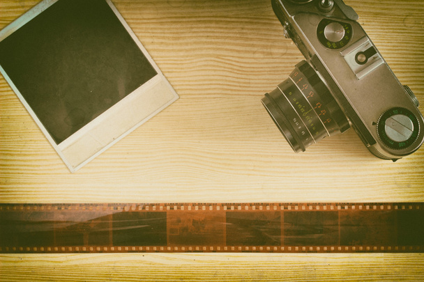 De camera en de foto met tape film liggen op een houten achtergrond. Een collage van herinneringen op film. Bovenaanzicht. Retro stijl - Foto, afbeelding
