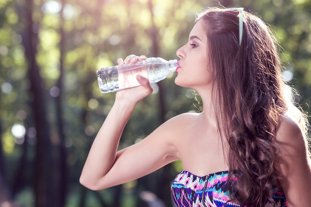 女の子は自然にボトルから水を飲む - 写真・画像