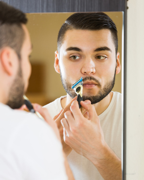 Man looking at mirror and shaving face  - Foto, Imagem