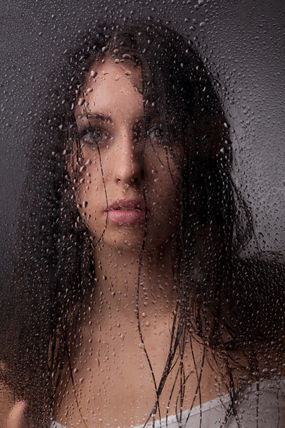 A beautiful girl on a black background behind the glass. - Zdjęcie, obraz