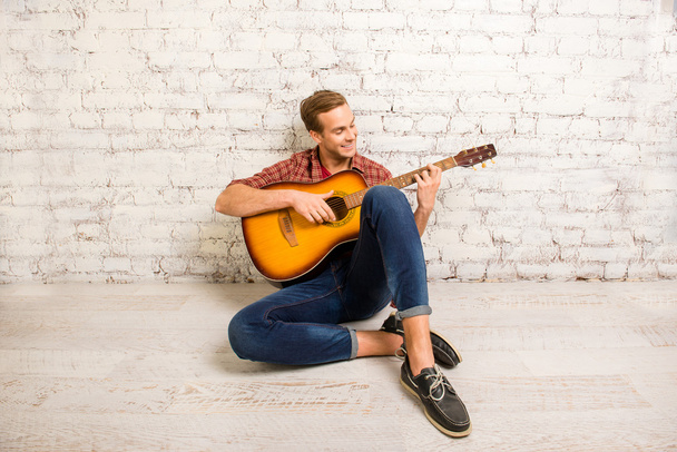 Handsome man  siting on floor and playing on the guitar - Fotografie, Obrázek