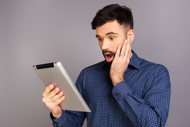 Portrait of shocked young man reading news on tablet - 写真・画像
