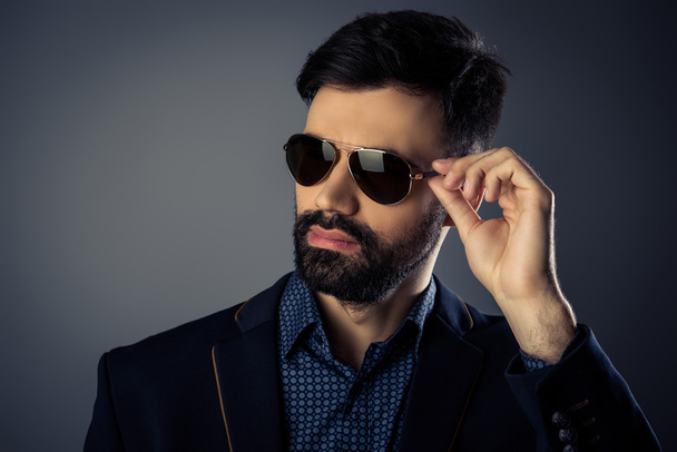 Attractive bearded man in suit touching his glasses - Fotó, kép