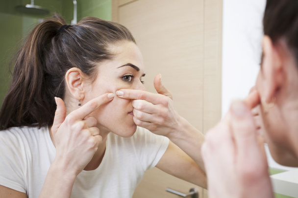Mujer joven aprieta su acné delante del espejo. Problemas de la piel, colmena de mujer
 - Foto, Imagen