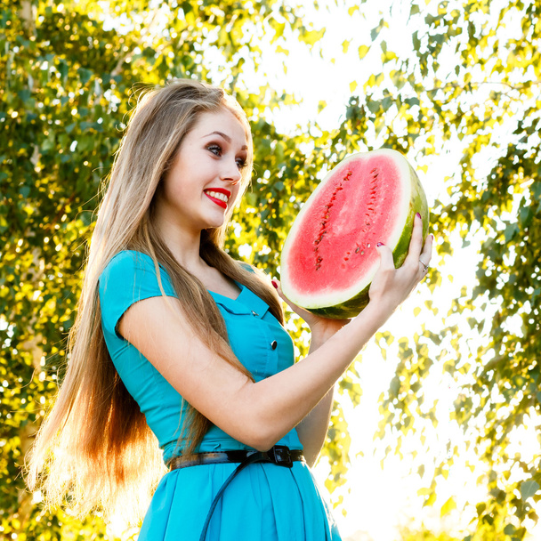 Beautiful blonde girl with long hair holds a half of watermelon - Foto, Imagen