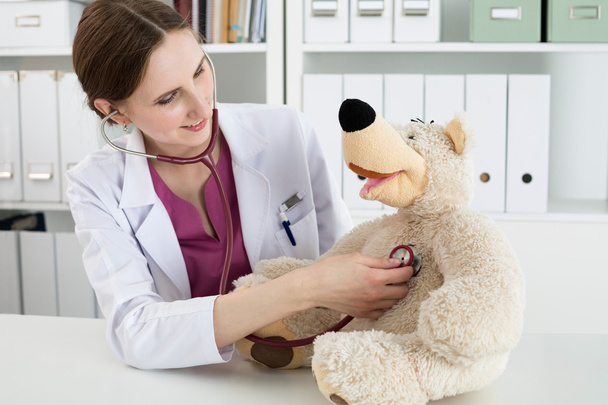 schöne lächelnde Ärztin im weißen Mantel untersucht Teddybär - Foto, Bild