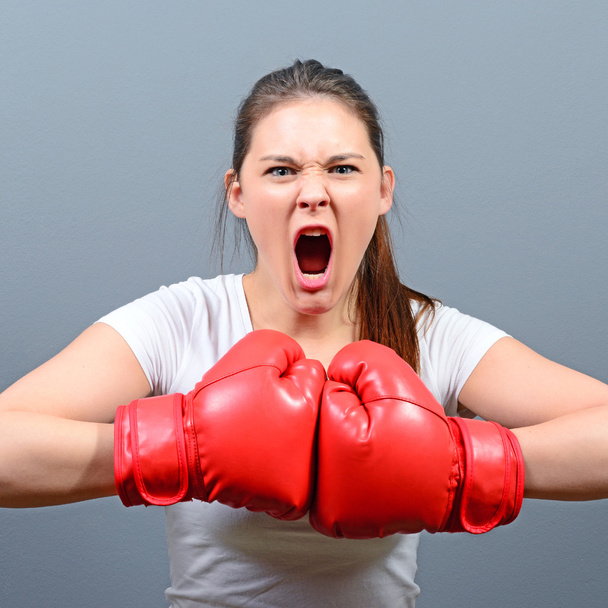 Portrait of angry woman posing with boxing gloves against gray b - Fotografie, Obrázek
