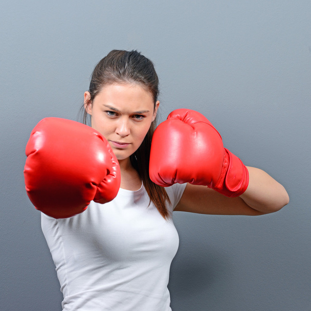 Portrait of young woman posing with boxing gloves against gray b - Foto, imagen