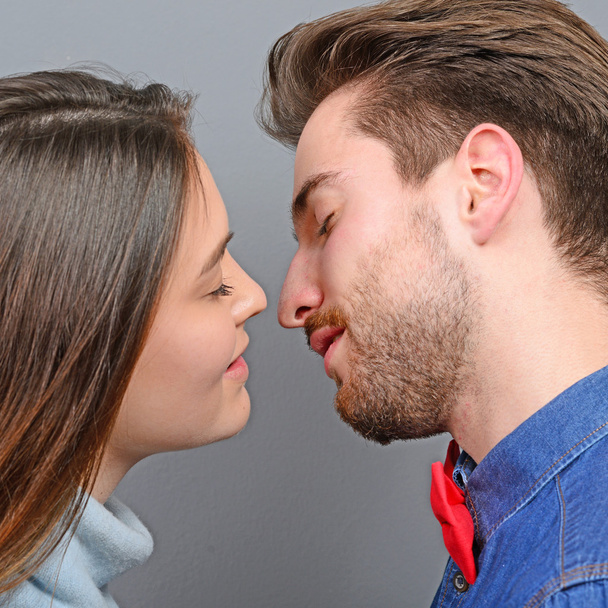Νεαρό ζευγάρι κοινή χρήση ειδύλλιο και φιλιά γκρι φόντο - Φωτογραφία, εικόνα