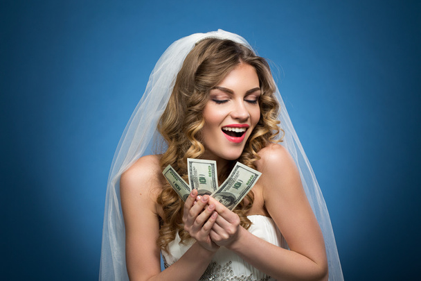 young beautiful girl in wedding dress veil with dollars in hands on blue background - Foto, Imagem