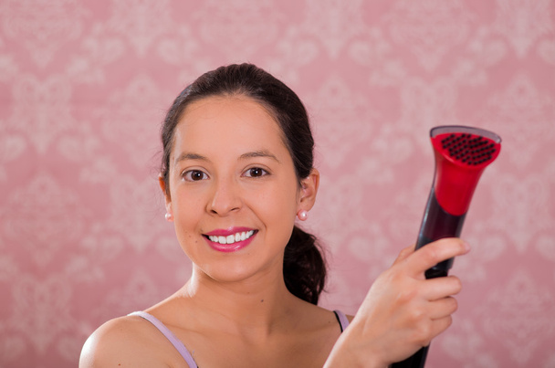 Brunette woman holding plastic nozzle of steam cleaning machine, smiling to camera, pink background - Fotó, kép