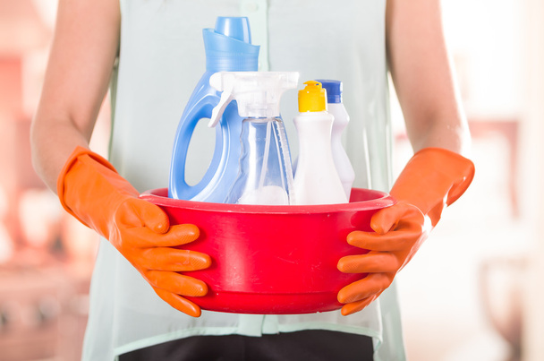 Closeup orange gloves holding red bucket of cleaning products and smiling to camera, housecleaning concept - Foto, Imagen