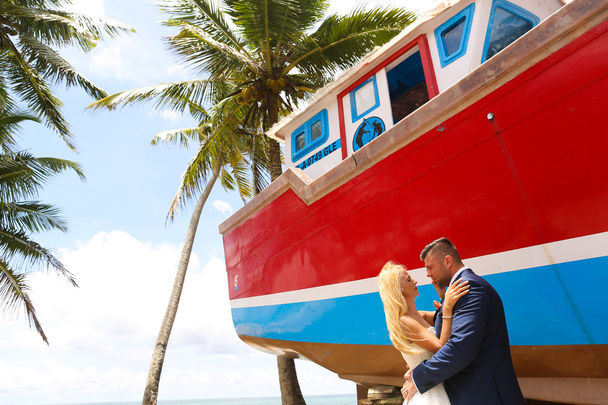 groom and bride kissing on the beach near a wooden boat - Φωτογραφία, εικόνα