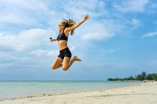 Jonge sportieve vrouw springen op een tropisch strand - Foto, afbeelding
