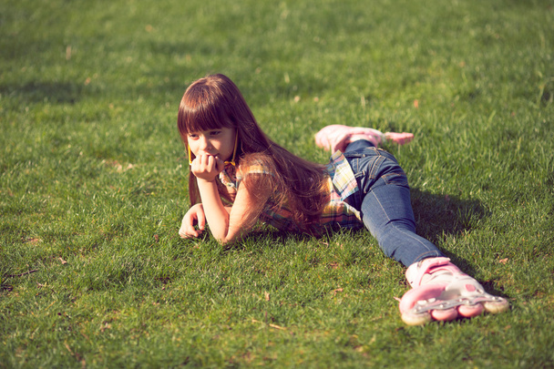 dziewczyna sobie Wrotki, siedząc na trawie w parku. - Zdjęcie, obraz
