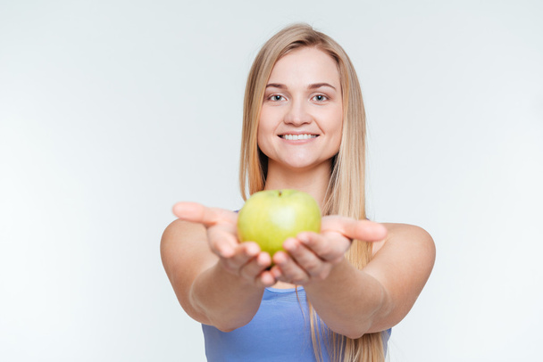 Smiling fitness woman giving apple at camera - Foto, afbeelding