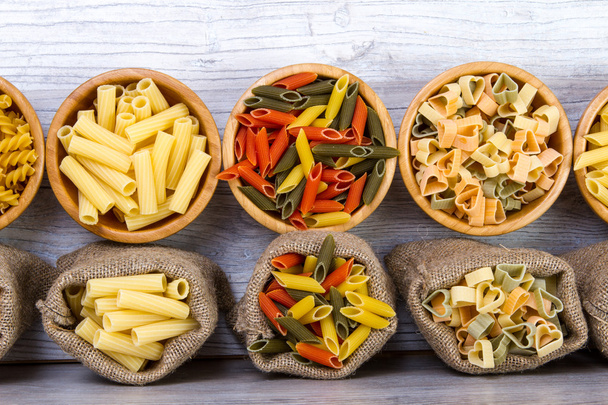 Various combinations of pasta on wooden background, burlap bags, bamboo bowls. diet and nutritional concept. - Фото, изображение